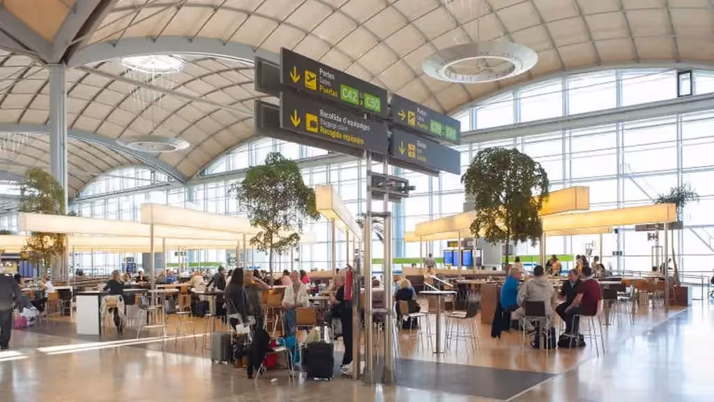 aena-aeroport-alicante-elche-medsestry-skoraya-pomoshch-zima-ru Пассажиры с багажом рядом с указателями выходов на посадку внутри терминала аэропорта