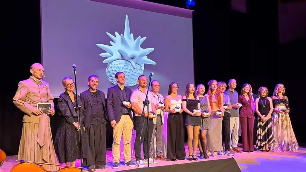 A group poses with awards on a stage in front of a projected sculpture