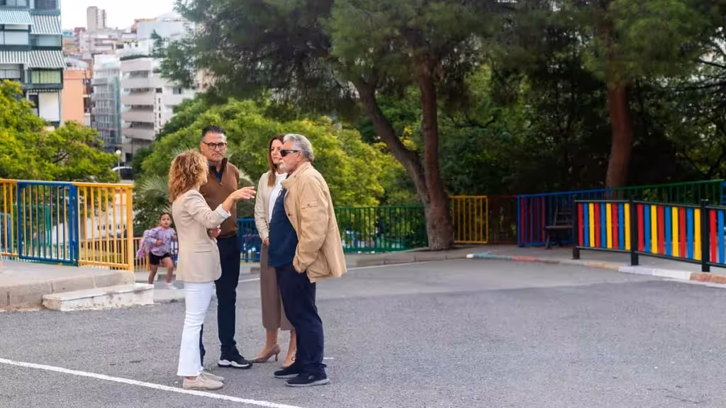 Benidorm plantará cien árboles en tres colegios durante las fiestas patronales Varias personas conversan en un patio escolar con árboles y vallas de colores