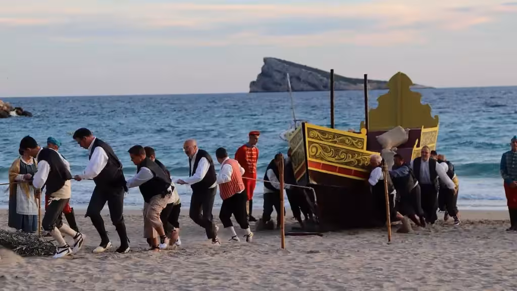 Teilnehmer in traditionellen Kostümen ziehen ein Boot über den Sand eines Strandes