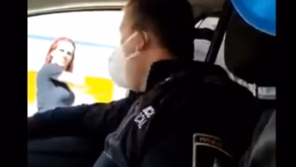 Videostandbild mit einem uniformierten Polizisten im Fahrzeug und einer Person außerhalb