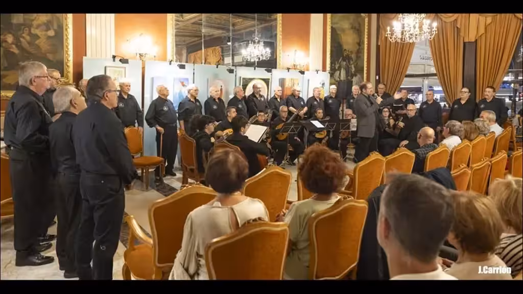 Chormitglieder und sitzende Musiker treten vor Publikum im Saal des Casinos auf.