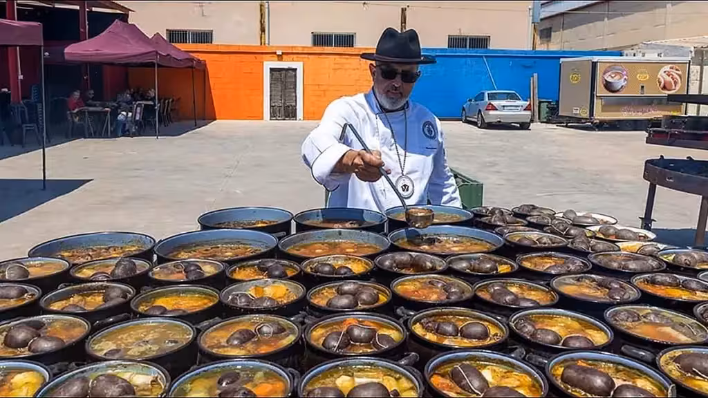 cocido-reposado-torrevieja-24-october-menu-bookings-en A cook serving broth beside numerous dishes of cocido in a courtyard