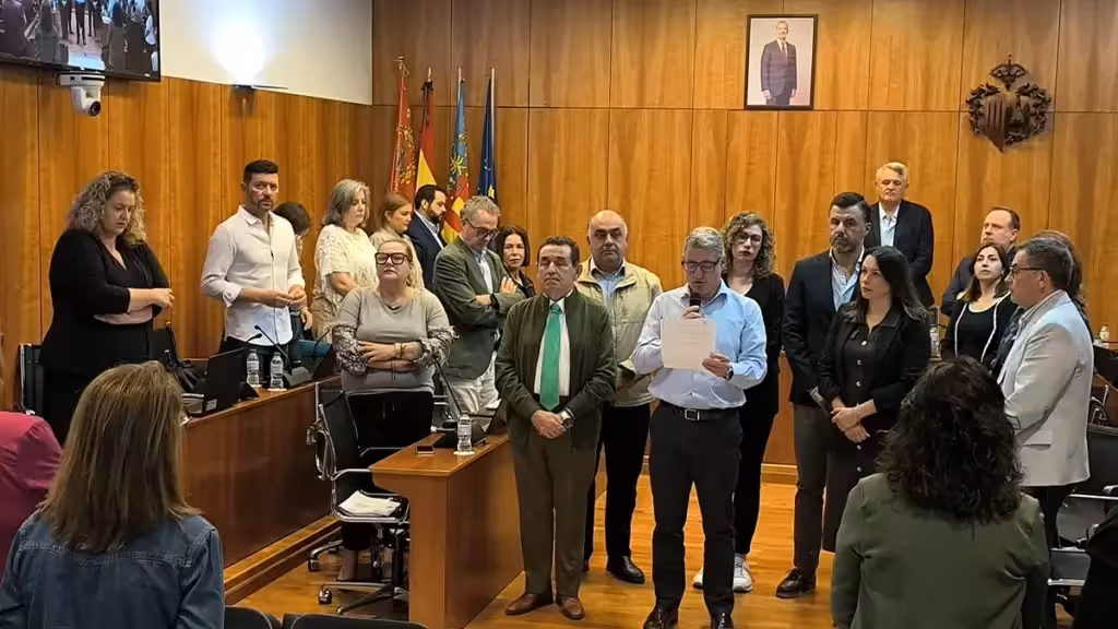 Grupo de personas de pie en el salón de plenos de Orihuela, una de ellas con un micrófono y un papel