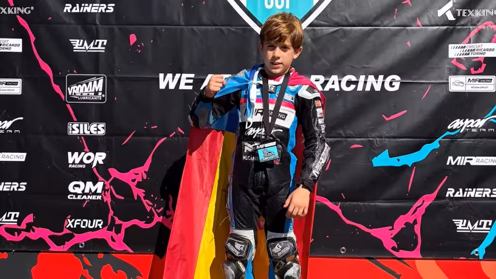 Junger Motorradfahrer im Rennanzug mit spanischer Flagge vor der Kulisse des MIR Racing Aspar Cup