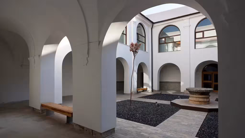 Patio con arcos blancos, bancos y un brocal de piedra en la Biblioteca María Moliner