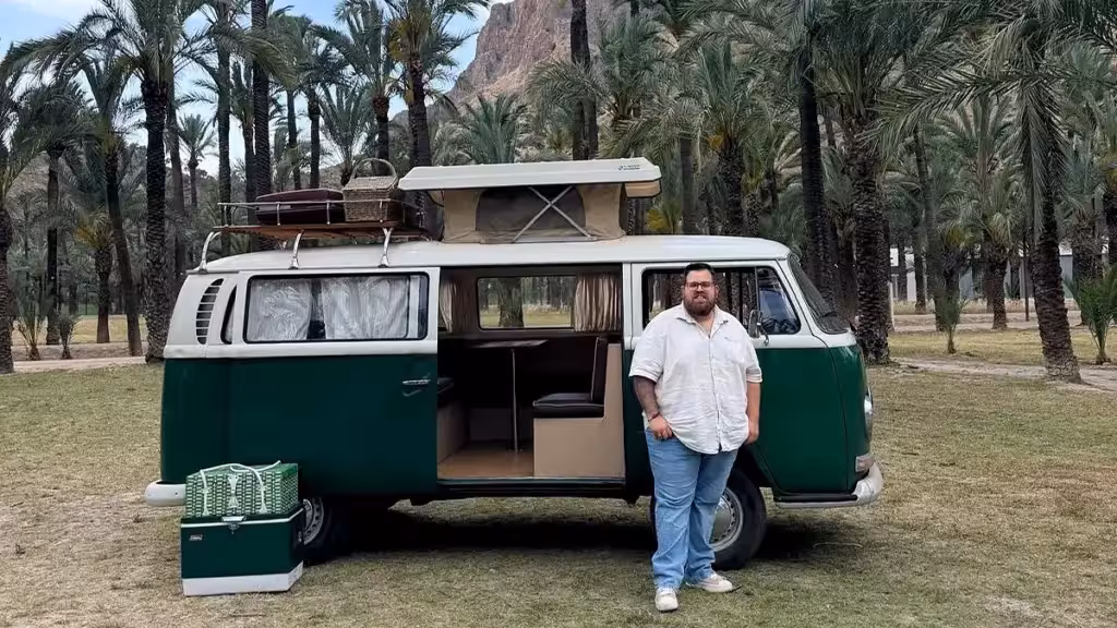 Ein Mann neben einem grün-weißen Campingbus zwischen Palmen auf dem Bild zur Sendung Caravana Educativa.