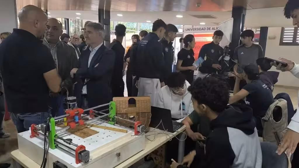 Teilnehmende und Besucher neben einer Maschine und Computern an einem Messestand.
