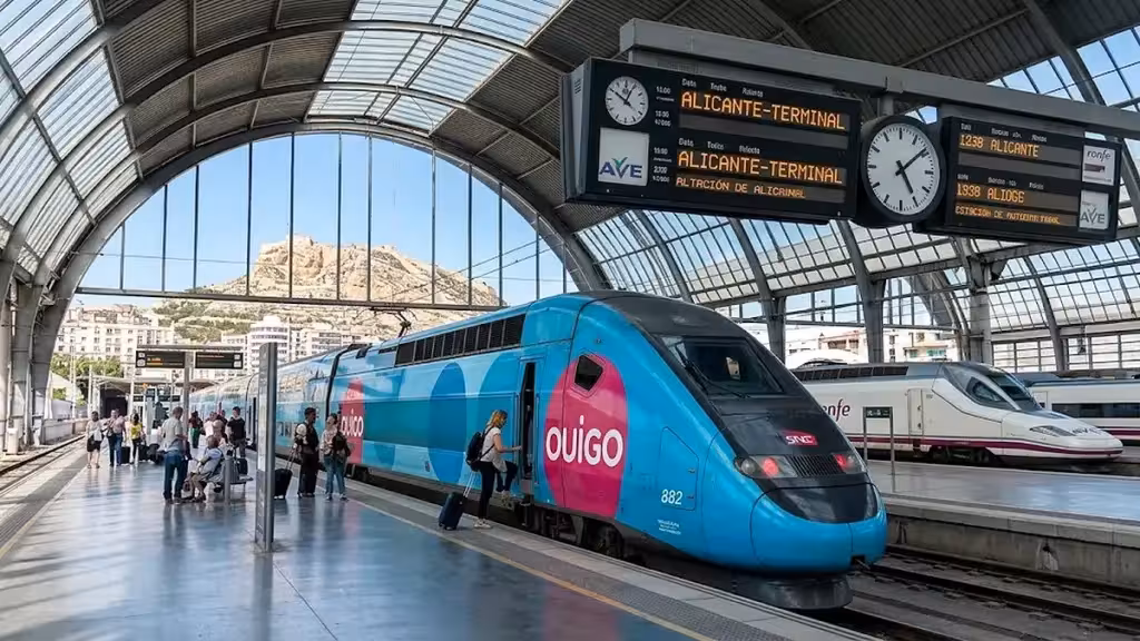 Tren Ouigo azul y rosa junto a un andén cubierto con paneles de Alicante-Terminal, en una imagen de archivo