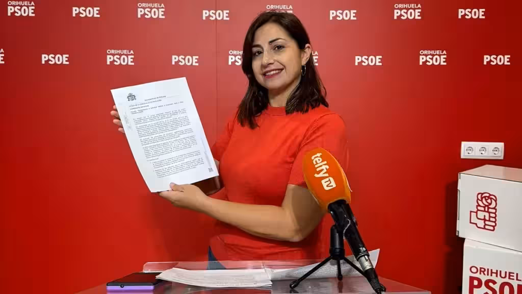 Женщина показывает документ у микрофона на фоне символики PSOE в Ориуэле