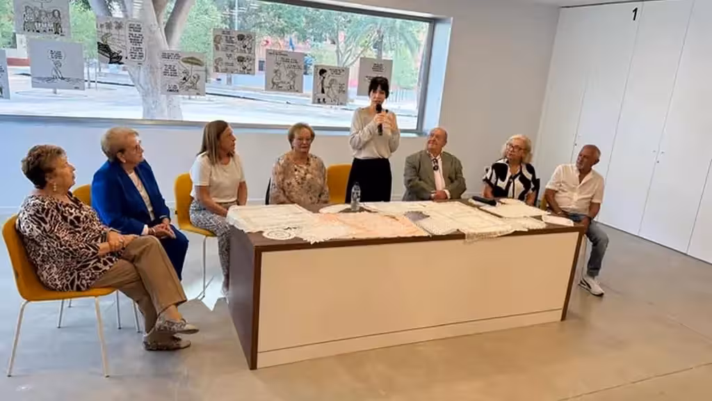 Участники встречи в Сан-Хавьере за столом на фоне выставленных в окне рисунков