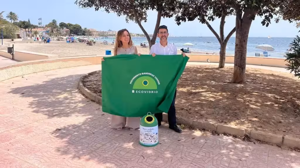 san-javier-zelenyy-flag-301580-kilogrammov-stekla-leto-2026-ru Два человека держат зелёный флаг Ecovidrio рядом с пляжем