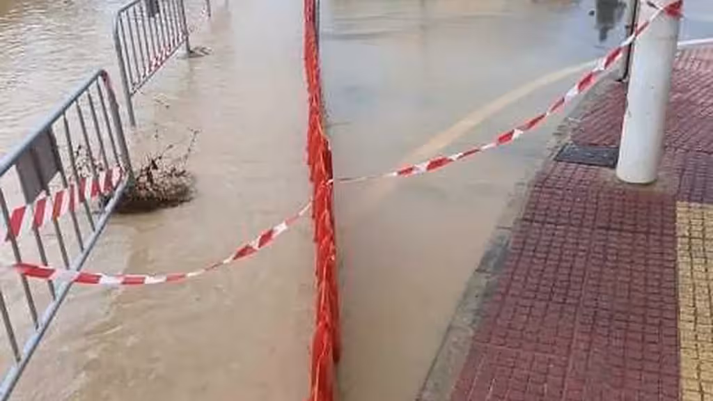 Überflutete Straße in El Mojón mit Metallgittern, Absperrband und einer roten Barriere
