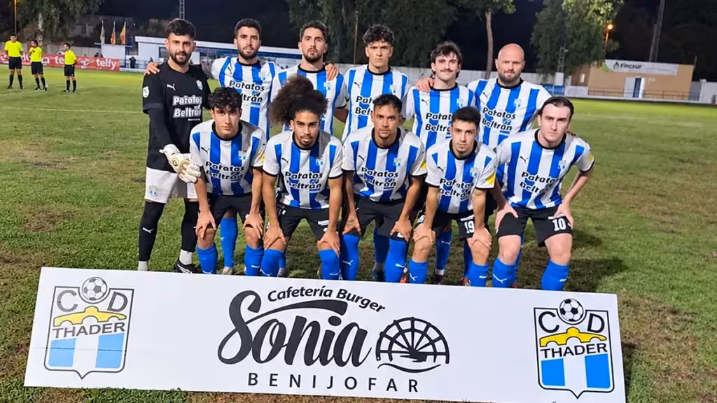 thader-rayo-ibense-gol-borja-segunda-victoria-rojales-es Futbolistas con camisetas a rayas azules y blancas posan en un campo iluminado tras un cartel del CD Thader