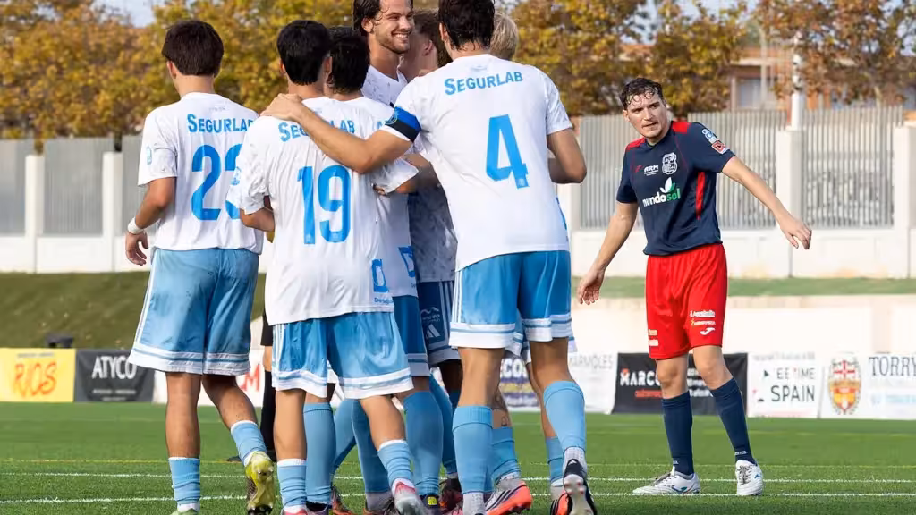 Footballers in white and blue gathered on the pitch beside a player in blue and red