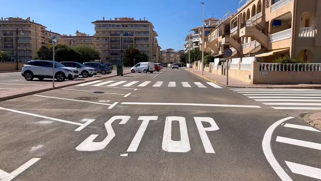 Cruce urbano con una marca de STOP, pasos de peatones y plazas de aparcamiento señalizadas
